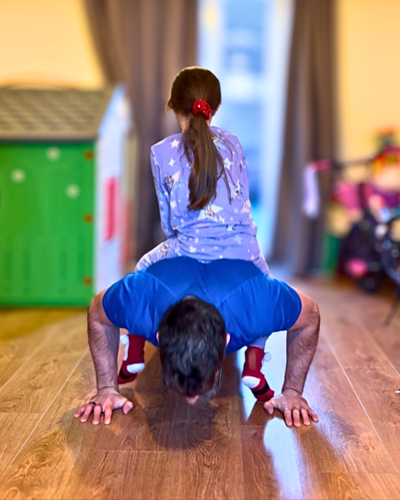 Dad performing a press up with his daughter on his back, playful and fun exercise